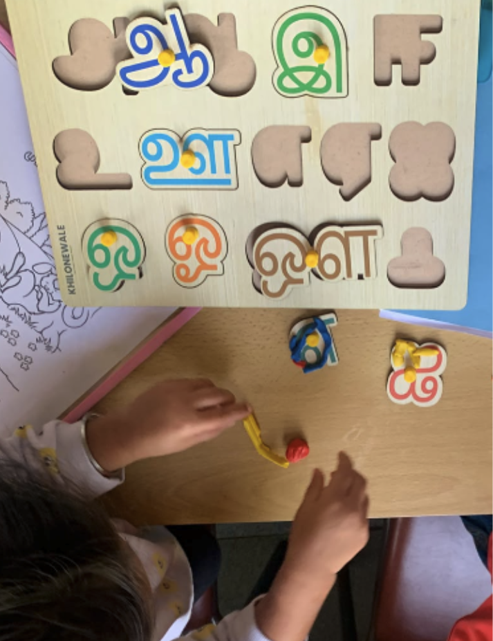 Child playing with a Tamil letter puzzle at a classroom table